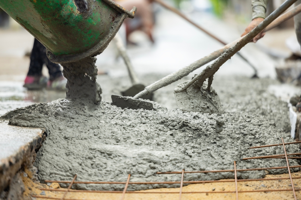 Mixer truck pouring cement concrete casting on reinforcing metal bars of sidewalk